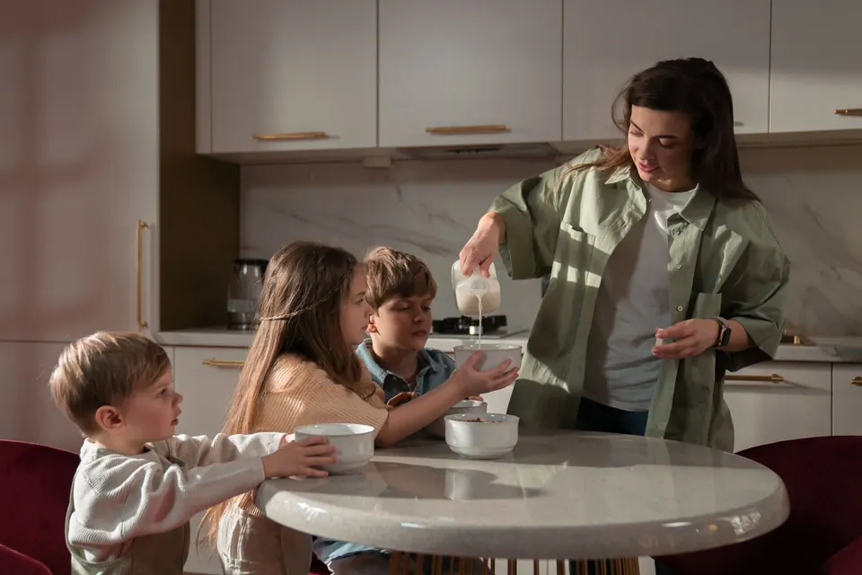 Een moeder schenkt melk in de ontbijtkommen van haar drie kinderen aan de keukentafel